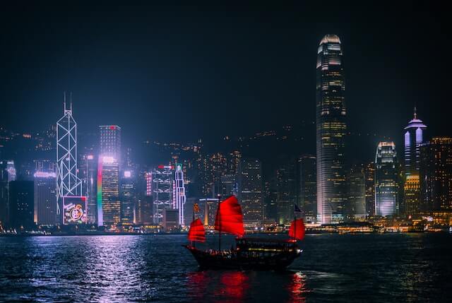 Hong Kong skyline in behind a body of water with a boat with red sails.